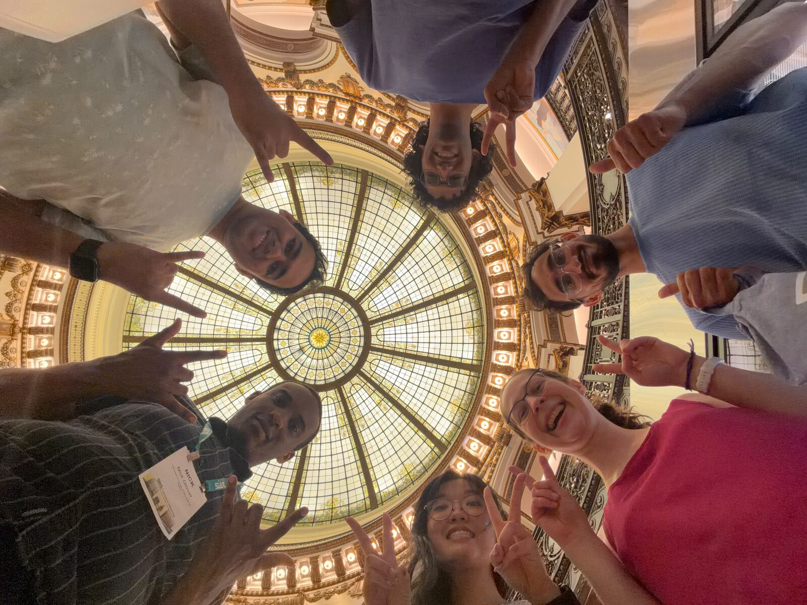 Looking-up group selfie of Aneesh and friends in a circle beneath a stained-glass dome