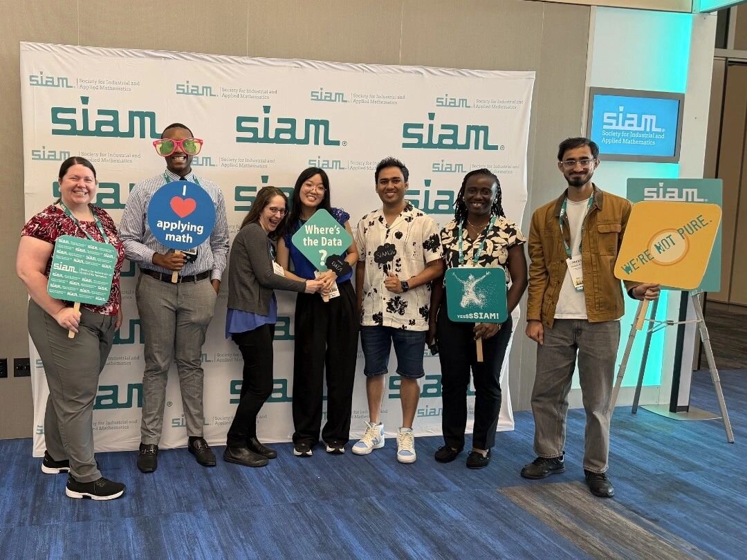 Aneesh with labmates and friends holding SIAM photo-booth signs at SIAM LS26